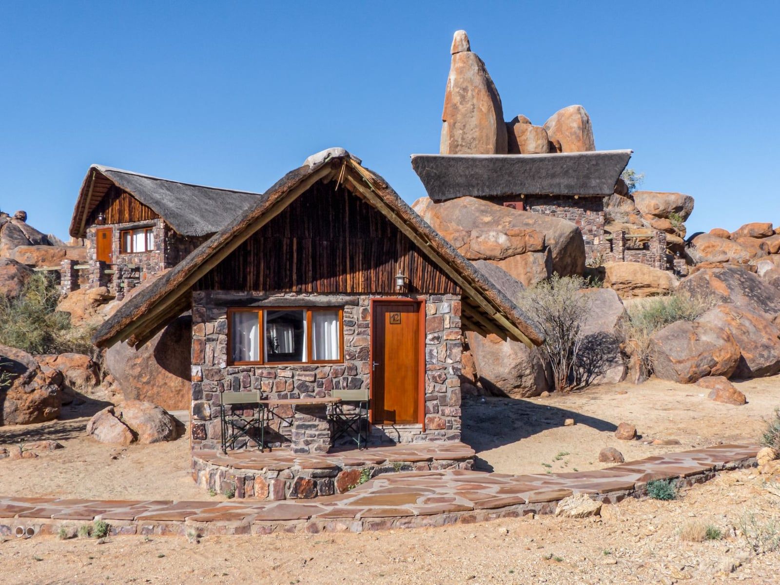 Chalés de piedra con tejados de paja enclavados entre rocas de granito en un lodge de safari del desierto de Namibia.